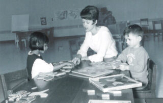 black and white image of woman with two children looking at books on table