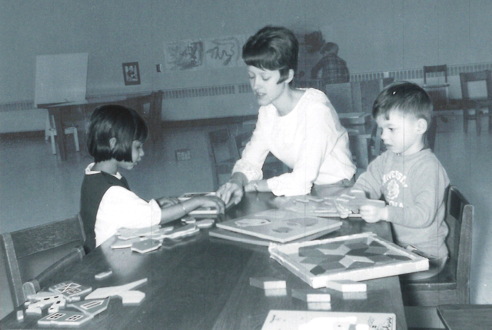 black and white image of woman with two children looking at books on table