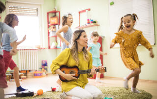 Children dancing around woman educator playing guitar