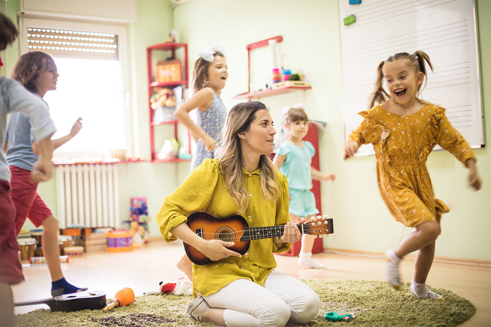 Children dancing around woman educator playing guitar