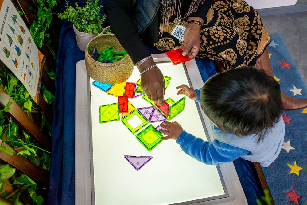 Educator and child building with blocks on a light table